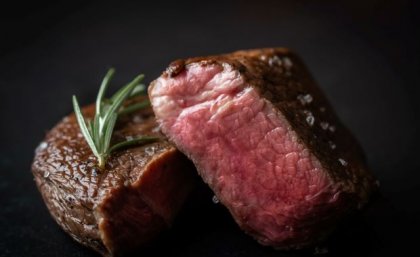 A close up image of two thick beef steaks, cooked with pink insides and some rosemary on a plate.